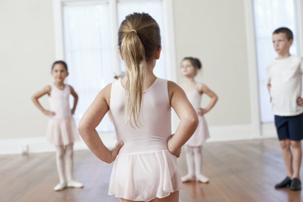Four children practicing ballet with hands on hips in ballet school